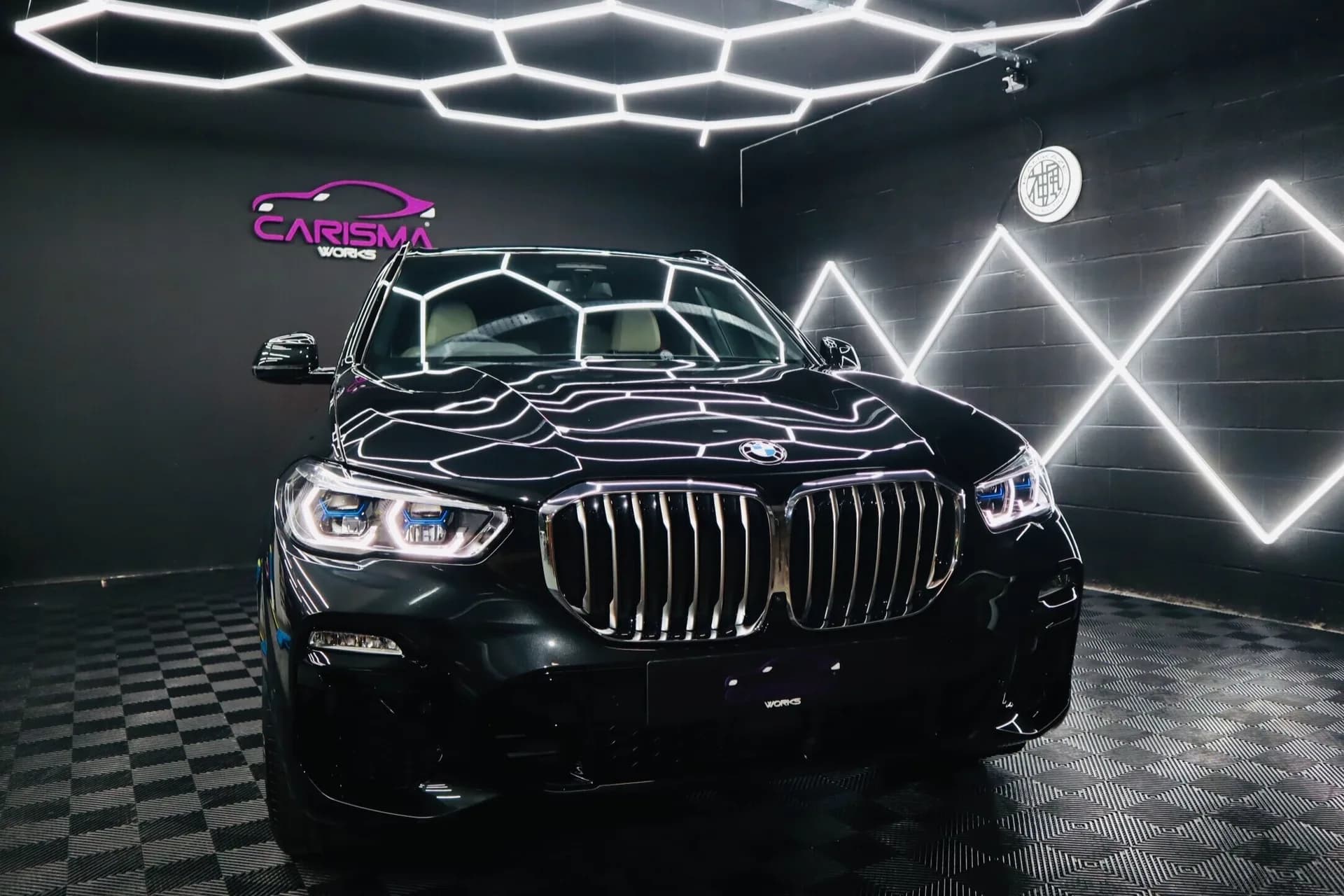 Black BMW X5 inside the Carisma Works detailing studio, branded neon signage on the wall